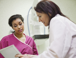 A doctor talks to a robed patient after her mammogram